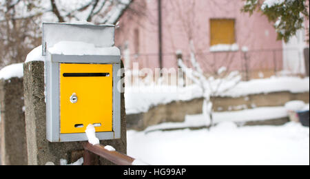 Coperta di neve giallo nella cassetta postale di fronte a una casa Foto Stock