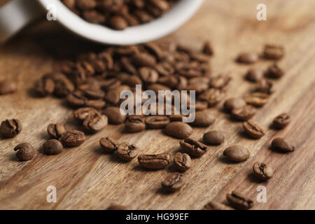 Rovesciato tazza cappuccino con chicchi di caffè tostati sulla tavola di legno Foto Stock