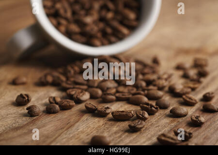 Rovesciato tazza cappuccino con chicchi di caffè tostati sulla tavola di legno Foto Stock