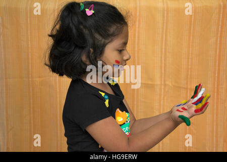 Grazioso piccolo ragazza indiana guardando le mani dipinte con colori Foto Stock