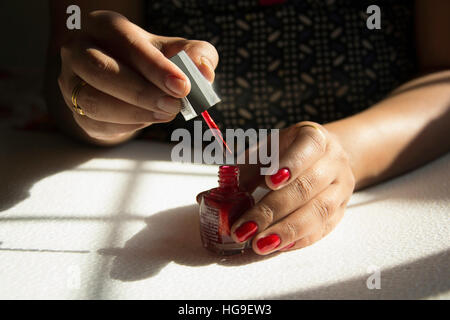 Giovane donna pittura i suoi chiodi con rosso smalto per unghie Foto Stock