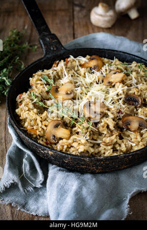 Risotto ai funghi con formaggio grattugiato in ghisa esperti su tavola in legno rustico. Verticale, vista ravvicinata Foto Stock