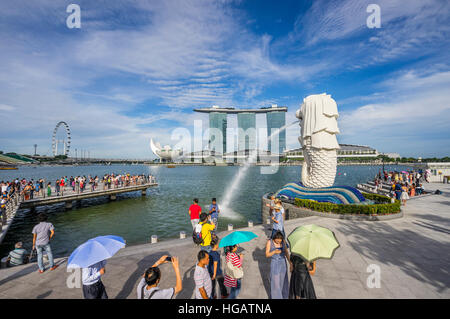 Singapore, Marina Bay, ai turisti di ammirare l'acqua sgorga statua Merlion contro lo sfondo della Marina Bay Sands Resort und il Singapore Flyer Foto Stock