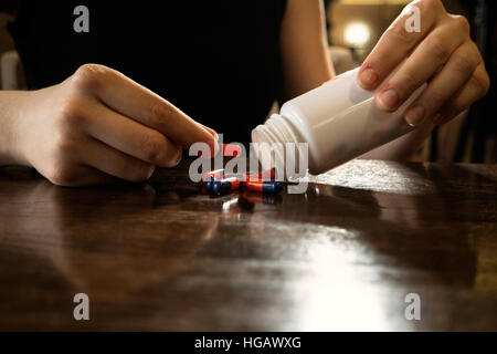 Donna uscire pillole dalla bottiglia di plastica bianca sulla tabella pilished Foto Stock
