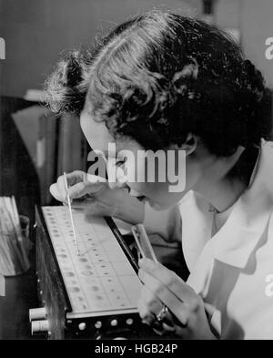 Tecnico di laboratorio la visualizzazione di campione ematico durante la digitazione, 1957. Foto Stock