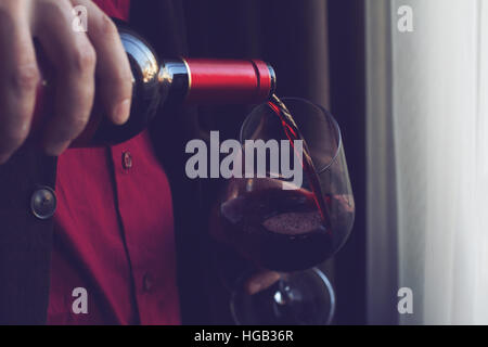 Chiudere orizzontale di uomo caucasico in abito nero e camicia versando il vino rosso in un bicchiere alto in un bar Foto Stock