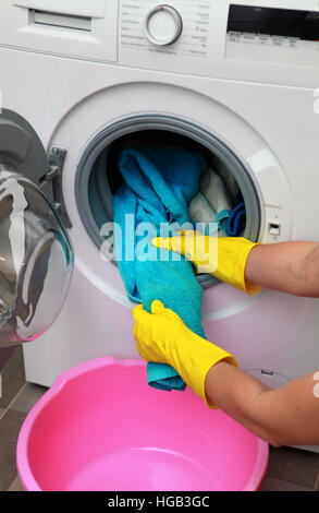 La donna le mani nei guanti di prendere i vestiti di colore dalla macchina di lavaggio Foto Stock