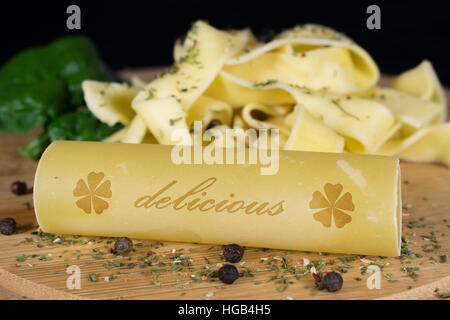 Su una tavola di legno è in primo piano un cannelloni con le scritte - deliziosa -, in background sono ulteriormente tagliatelle guarnite con foglie spinac Foto Stock