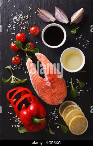 Raw bistecca di salmone e gli ingredienti su un nero tagliere. verticale vista superiore Foto Stock