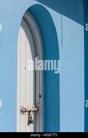 Round bloccato lo sportello superiore. Un bloccato porta bianca con un round top in un dipinto di blu edificio in stucco. Una pesante chiavistello blocca lo sportello. Hopetown, Foto Stock