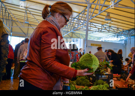 Donna di ispezionare un cavolo cappuccio in un mercato contadino Foto Stock