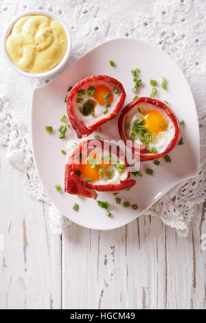 Uova fritte avvolto in pancetta croccante su una piastra con la salsa sul tavolo. verticale vista superiore Foto Stock