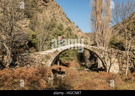 Un escursionista cammina su un antico in pietra ponte genovese attraversare un torrente di montagna di Tartagine in Corsica Foto Stock
