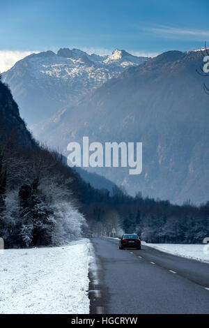 Strada che corre attraverso il paesaggio innevato verso le montagne con auto Foto Stock