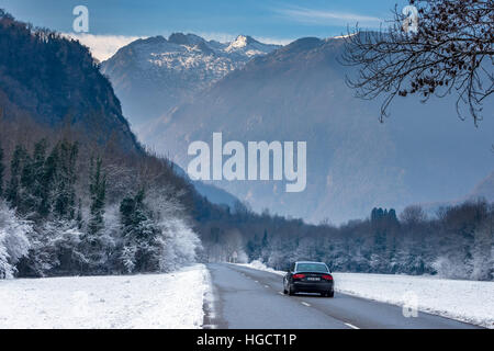 Strada che corre attraverso il paesaggio innevato verso le montagne con auto Foto Stock