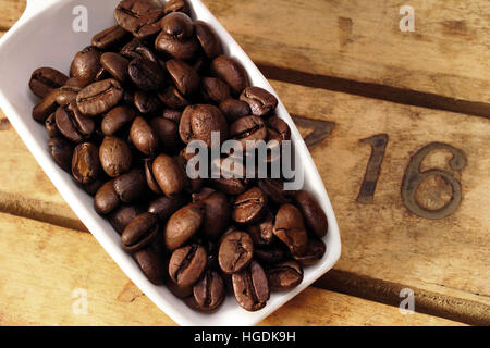 Scoop bianco riempito con i chicchi di caffè sulla parte superiore dei pannelli in legno Foto Stock