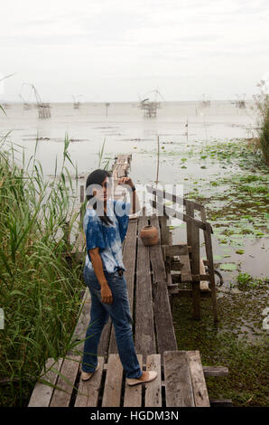 Traveler donna asiatica in posa e in piedi sul ponte di legno e viaggi Pakpra canal al divieto di Pra Pak di villaggio di pescatori nel tempo del tramonto a Phatthalung Foto Stock