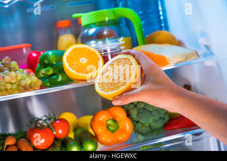 La donna prende l'arancione dal frigorifero aperto. Cibo sano. Foto Stock