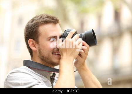 Vista laterale di un uomo felice fotografare con una fotocamera reflex digitale per la strada di una città o di un comune Foto Stock