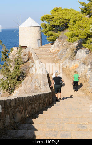 La gente a piedi il sentiero costiero verso un vecchio mulino in pietra, Spilia, Hydra, ISOLE DELL'ARGOSARONICO Grecia Foto Stock