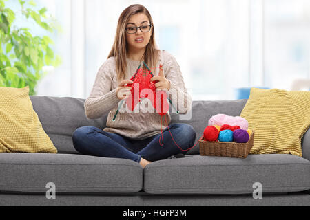 Confuso giovane donna seduta su un divano e di lavorazione a maglia Foto Stock