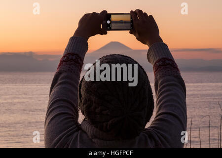 Una donna giapponese utilizza un iphone per scattare una foto del Monte Fuji durante l'ultimo tramonto del 2016. Muira, Kanagawa, Giappone Foto Stock