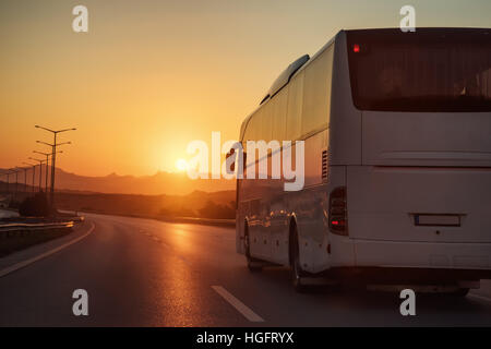 Bus bianco in marcia su una strada verso il sole di setting Foto Stock
