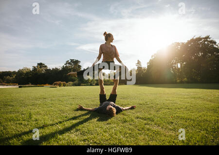 Montare la coppia giovane facendo acroyoga sull'erba. L uomo e la donna nel parco coppia pratica yoga pone nella mattina di sole. Foto Stock