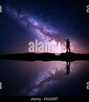 Via Lattea. Silhouette di un uomo in piedi puntando il dito nella notte cielo stellato sulla montagna vicino al fiume Foto Stock