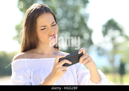 Stupiti ragazza giochi on line con uno smart phone in un parco Foto Stock