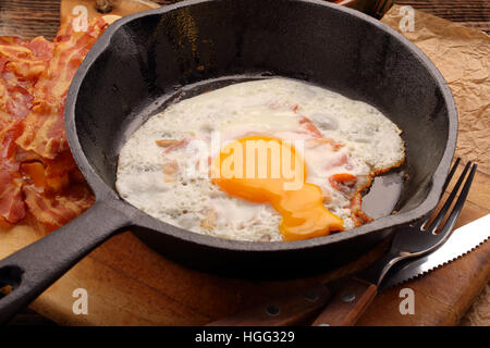 Uovo fritto a caldo con pezzi di pancetta in una padella in ghisa Foto Stock