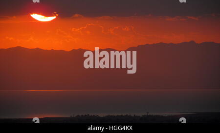 Rosso riflette la luce del sole fuori del Salton Sea un inizio di mattina con il cioccolato montagne sullo sfondo Foto Stock