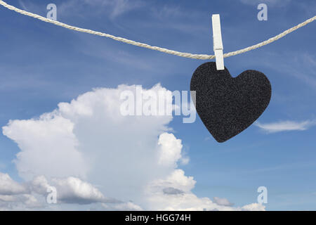 Cuore nero appeso sulla corda di canapa sul cielo blu di sfondo e avere copia spazio per gestire il testo che si desidera. Foto Stock