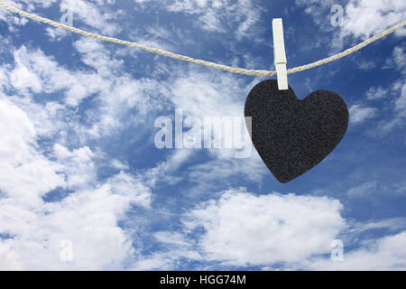 Cuore nero appeso sulla corda di canapa sul cielo blu di sfondo e avere copia spazio per gestire il testo che si desidera. Foto Stock