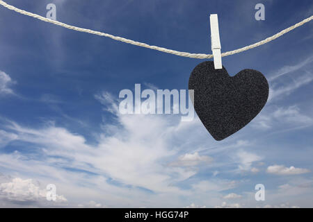 Cuore nero appeso sulla corda di canapa sul cielo blu di sfondo e avere copia spazio per gestire il testo che si desidera. Foto Stock