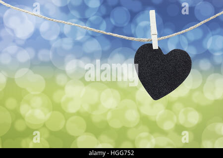 Cuore nero appeso sulla corda di canapa su abstract colorato sfondo bokeh di fondo e hanno spazio copia per gestire il testo che si desidera. Foto Stock