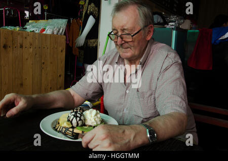 Il tedesco vecchio uomo mangiare il miele e il cioccolato sulla lava cialde con gelato alla vaniglia e di banana e panna montata nel mercato su Gennaio 7, 2017 in Nonthabu Foto Stock
