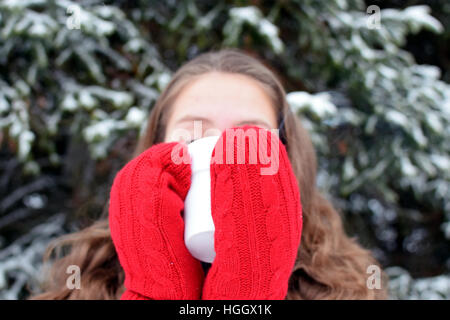 Giovane donna con red muffole di bere tè o caffè caldo in inverno sul all'esterno. Foto Stock