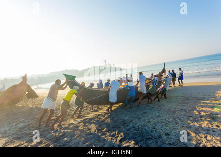 Comunità aiutando lo sforzo degli abitanti di un villaggio spingendo la pesca in barca insieme dalla spiaggia di sabbia in acqua sulla mattina di sole in Kovalam India Foto Stock