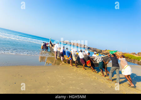 Comunità aiutando lo sforzo degli abitanti di un villaggio spingendo la pesca in barca insieme dalla spiaggia di sabbia in acqua su una mattina di sole in Kovalam, ke Foto Stock