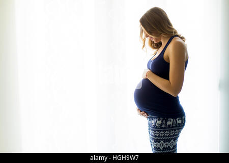 Piuttosto giovane donna incinta in piedi dalla finestra in camera Foto Stock