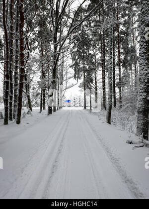 Auto tracce di pneumatici sulla strada invernale nella neve profonda nella foresta di solitario con cartelli stradali Foto Stock