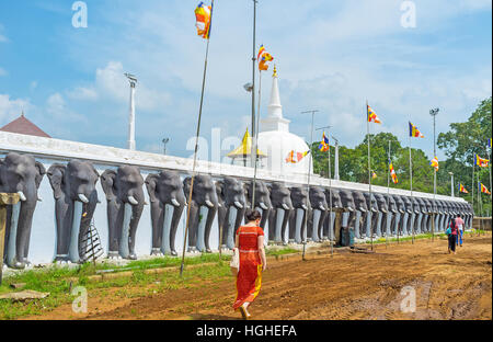 I visitatori a piedi lungo la recinzione, decorata con elefanti nero all'ingresso Ruwanwelisaya Stupa, Anuradhapura, Sri Lanka. Foto Stock