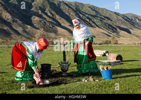 Il kazako donne in costumi nazionali cucinare la carne all'aria aperta, nel villaggio di soggiornare, Kazakistan Foto Stock