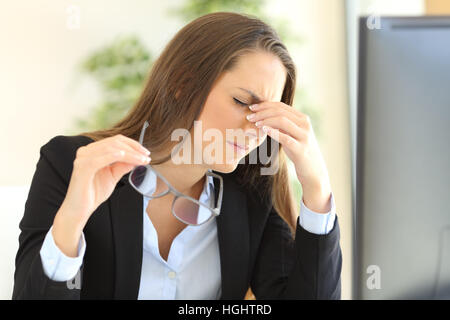 Affaticato imprenditrice azienda bicchieri sofferenza affaticamento degli occhi davanti a uno schermo PC in ufficio Foto Stock