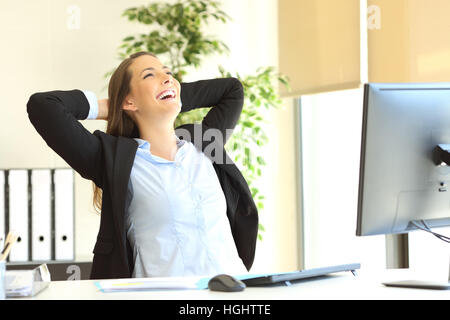 Soddisfatto imprenditrice con bracci sulla testa di ridere seduto su una sedia e rilassante in ufficio Foto Stock