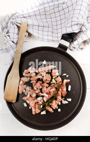 Il pollo crudo gulasch con cipolla, la spatola di legno e di timo in un tegame Foto Stock