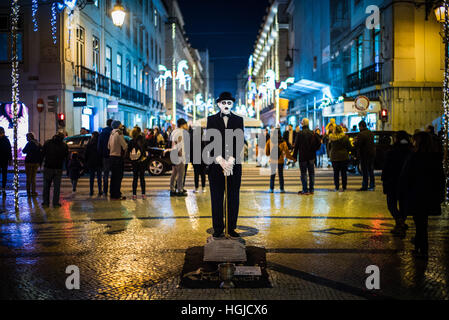 Un suonatore ambulante pone come un triste Charlie Chaplin su una serata umida in Rua Augusta, Lisbona, Portogallo Foto Stock