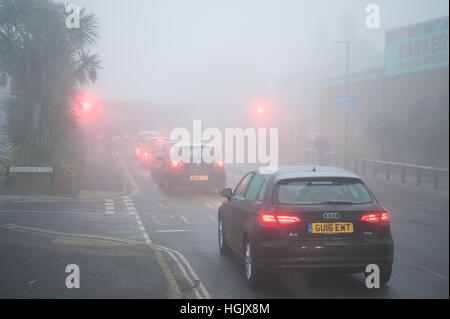 In una mattinata nebbiosa vetture di accodamento in attesa in una linea di traffico in corrispondenza di un passaggio a livello ferroviario nel West Sussex, in Inghilterra, Regno Unito. Foto Stock