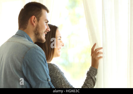 Affettuosa matrimonio aprendo le tende e guardando al di fuori attraverso una finestra in una nuova bellissima giornata con una luce calda Foto Stock